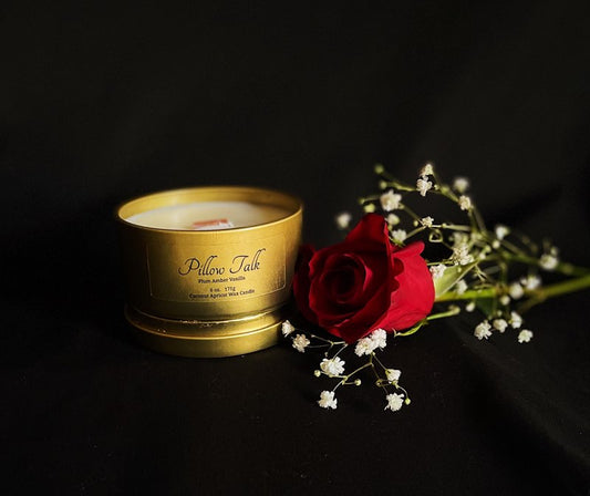 Pillow Talk Luxury coconut wax candle in a gold metal tin beside a red rose 